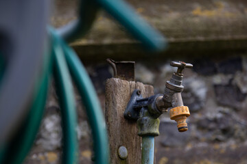 An old-fashioned garden tap with selective focus, blurred green hose in the foreground. Can be used as a symbol of water shortage