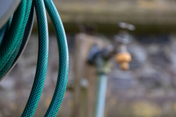 A garden scene with a coiled hose on a post, with a blurred background including a tap. Can be used...