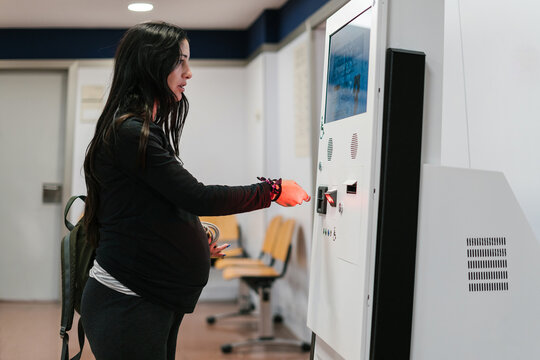 Young pregnant woman collecting queue token at machine