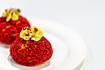 Exclusive red shu desserts with nut sprinkles and cream decoration in form of leaves on white plate on blurred white background. Modern cooking, restaurant menus, food design, culinary blog