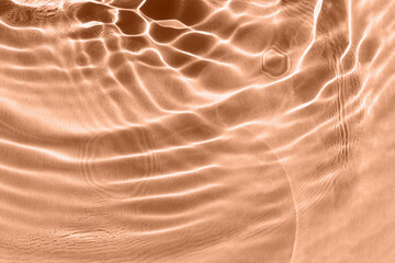 Textured background of peach water with sun reflections. Concept of tranquility and natural beauty. Closeup, selective focus, defocus. Color of year 2024