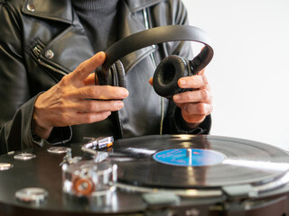 A lady wearing a leather jacket holding to use her headphones while her turntable is playing a...
