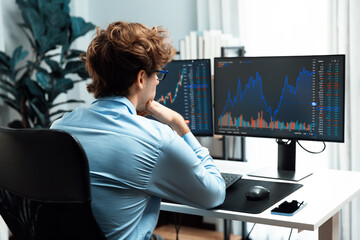 Young investor in stock trader looking on dynamic financial exchange investment on pc screen in current market graph, concentrating real time at modern office, analyzing statistic profit. Gusher. - obrazy, fototapety, plakaty