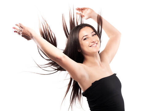 Young woman with long dark hair. Standing confidently in against white background throwing hair in the air.