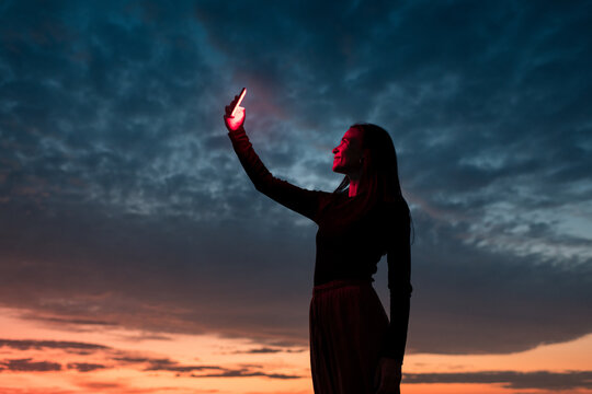 Standing woman holding up red luminous phone
