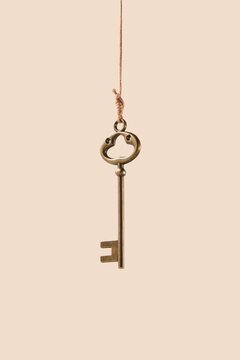 Bronze vintage key hanging on thread over beige background