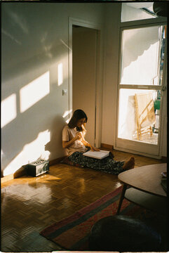 An analog image of a woman reading a book indoors in the sunlight