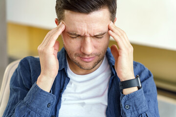 A man appears to be experiencing a headache or stress, his hands pressed against his temples in...