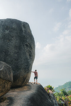 Man standing near the boulder overlooking a tropical island