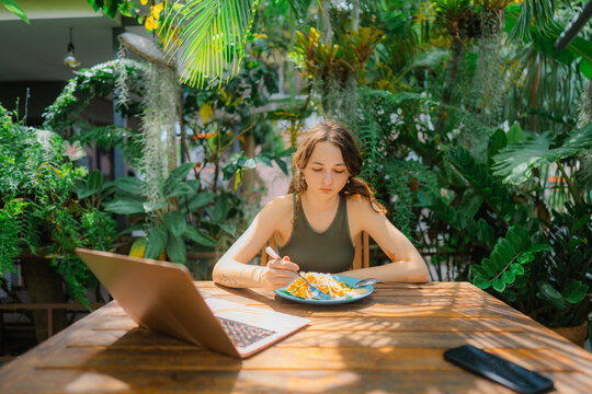 Woman eating noodle and using laptop 