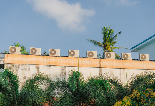 Air conditioners on the roof of asian building surrounded by palms 