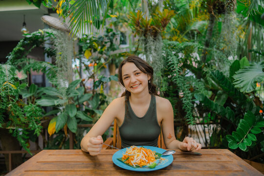 Woman eating pad thai in restaurant on the background of lush foliage
