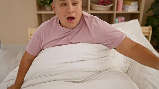 Terrifying nightmare sparks early morning wake-up scream for young, handsome latin man lying in bed, stretching arms, visibly scared in his homely bedroom's interior