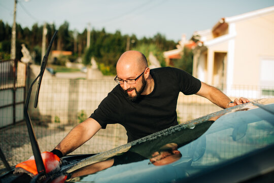 Man smiling while cleaning windshield of his car