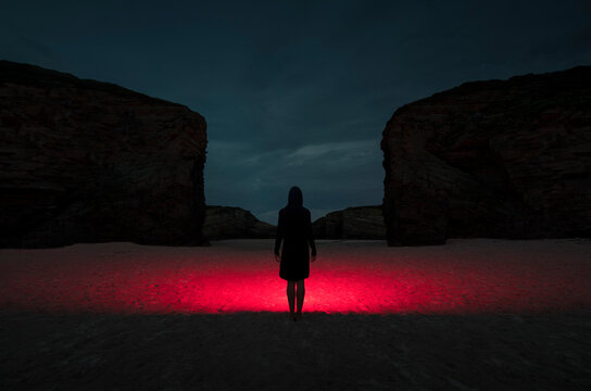 Surreal silhouette standing on red light beach at night