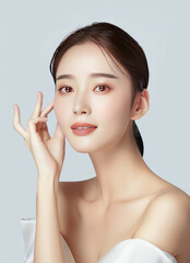 A beautiful asian woman with delicate skin, wearing white and touching her face in front of the camera on an isolated light gray background,generative ai