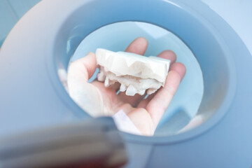 a hand holds a dental prosthesis model as seen through a large professional magnifying lens - obrazy, fototapety, plakaty