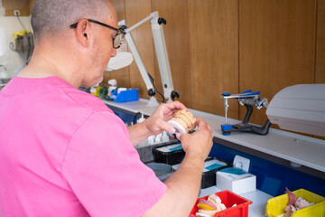 A dental technician observes in detail and holds a plaster cast of a complete denture to work on it.