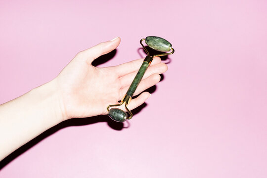 Beauty product photo of hand holding a green jade stone roller 