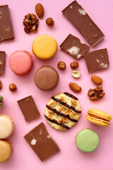 Pastel macarons, almond chocolate, peanut butter cookies and various nuts on bright pink background. Top view.