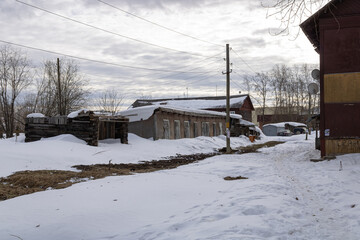 Buildings of old shabby houses in a provincial town in northern Russia. Corner of a house with satellite TV and advertising sheet, power pole with store advertisement, ruined barn.