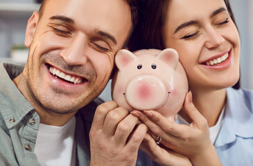 Close up of happy young family holding piggy bank indoors to save money for future. Married couple planning saving their budget together. Investments and financial freedom concept.