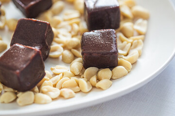 Gourmet Dark Chocolate Cubes Surrounded by Scattered Peanuts on White Plate