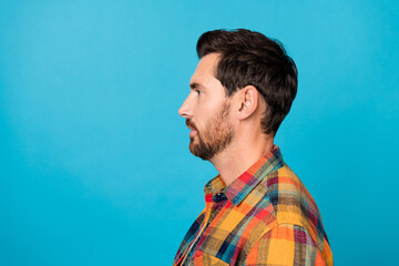 Side profile photo of serious handsome man with stylish beard dressed plaid shirt look at barbershop ad isolated on blue color background