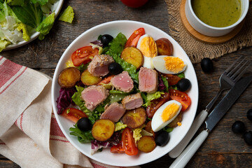 Fresh and healthy salad with vegetables and fried tuna, vegetables and potato slices, on a wooden background.