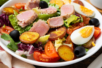 Fresh and healthy salad with vegetables and fried tuna, vegetables and potato slices, on a wooden background.
