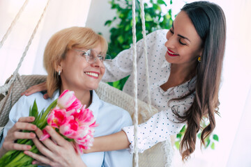 Happy mother and daughter in international women's day hugging each other and having fun with bouquet of tulips at home while celebrating holiday - 771004302