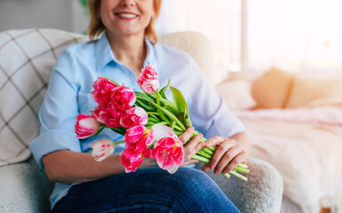 Close up image of female hands with bunch of tulips while she sitting on the chair at home. Mothers or women day - 771004357
