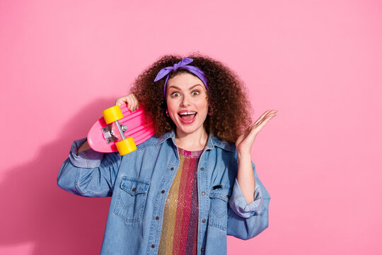 Photo of cheerful excited lady dressed denim outfit rising arm holding penny board empty space isolated pink color background