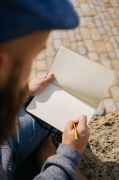 Unrecognizable man drawing in sketchbook on street