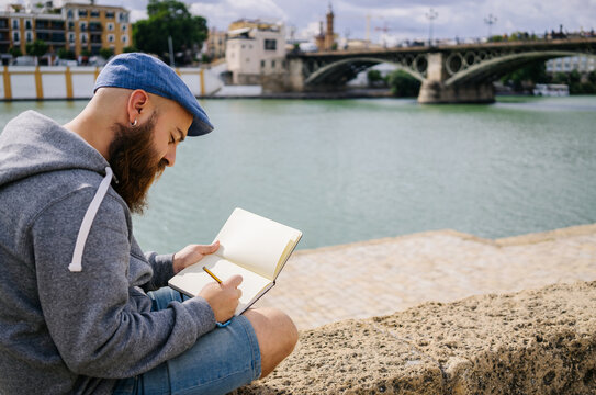 Focused illustrator drawing in sketchbook on riverside