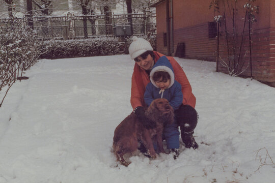 1979. Mom and son playing with their dog in a snowy garden.