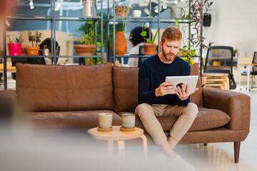 Young Professional on Sofa with Tablet in Modern Office.