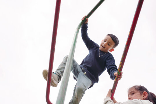 Low Angle View of Cute Children Climbing on Monkey Bar.