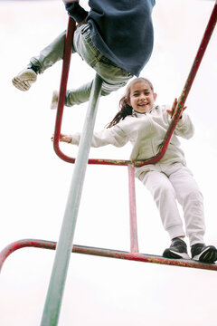 Low Angle View of Cute Children Hanging on Monkey Bar.