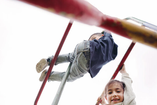 Low Angle View of Cute Children Hanging on Monkey Bar.