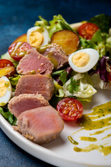 Delicious Nicoise salad with fried tuna, vegetables, lettuce and egg in a plate on a concrete background