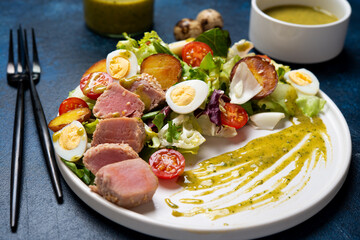 Delicious Nicoise salad with fried tuna, vegetables, lettuce and egg in a plate on a concrete background