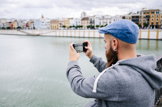 Young man taking photo of river by city on riverbank