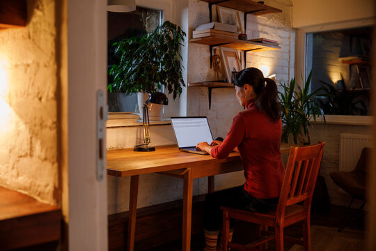 Businesswoman working on laptop at illuminated table in house