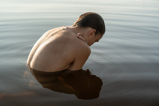 Wet topless model reflected on water surface while posing outdoo