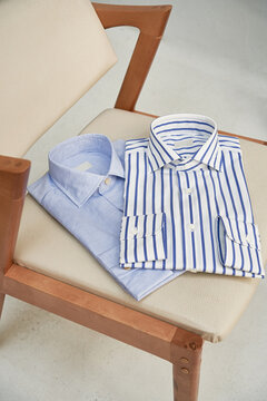 Two men's shirts lie on a beige armchair