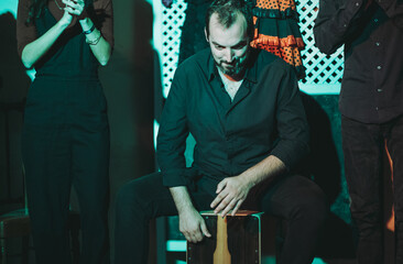 Stylish man sitting on Cajon box while drumming with band