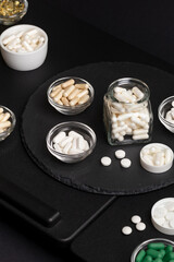Nutritional supplements  in jars on a black desk on a black background. Vitamins and minerals to...