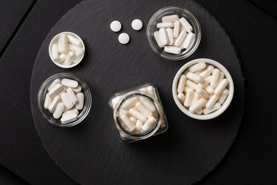 White colored nutritional supplements  in jars from above on a black desk on a black background. Vitamins and minerals to improve standard of living.