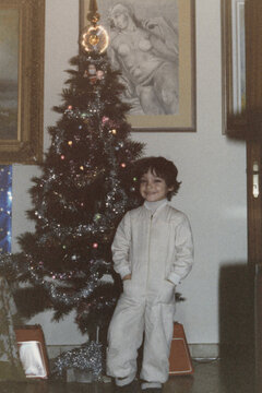 1983. Smiling child posed in front of the Christmas tree.
